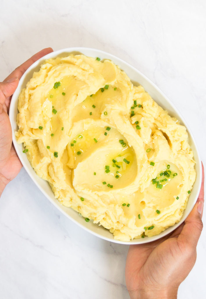 A woman holds a bowl of Instant Pot Mashed Potatoes garnished with butter and chives