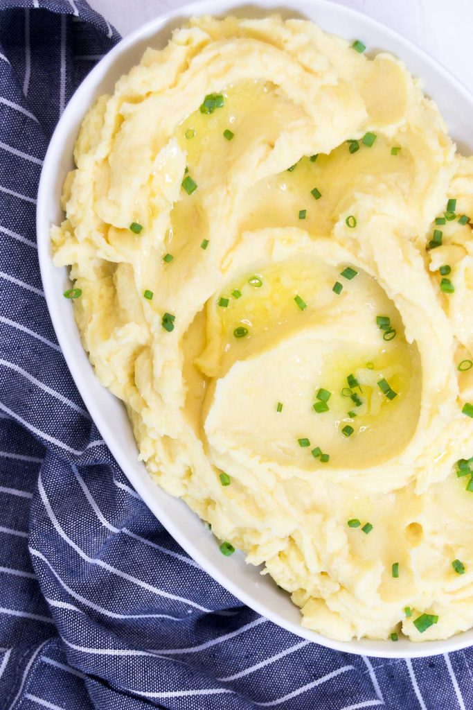 Close up of Instant Pot Garlic Mashed Potatoes in a bowl with chives and melted butter