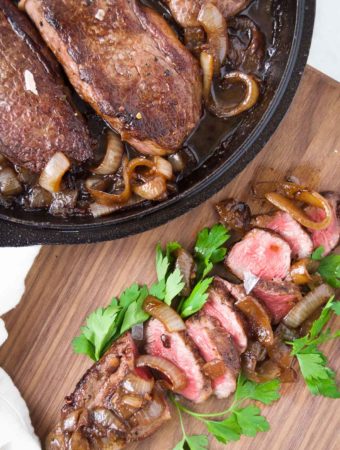 sliced steak with caramelized onions on a wooden cutting board
