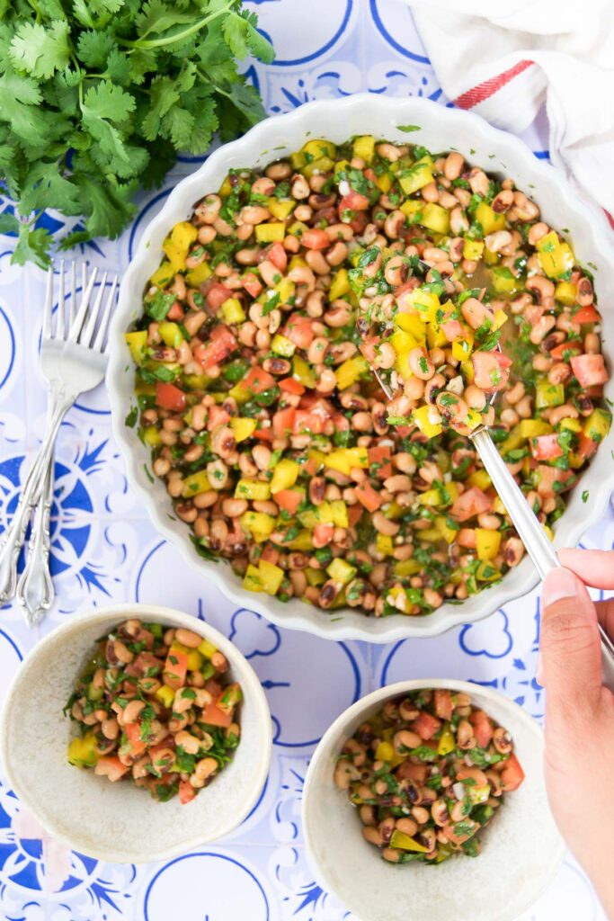 A woman scoops Black Eyed Peas salad recipe into bowls with a spoon