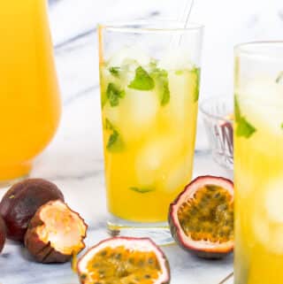 Two cups of passion fruit juice garnished with ice and mint next to purple passion fruit