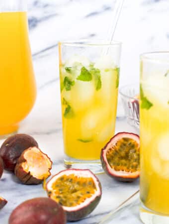 Two cups of passion fruit juice garnished with ice and mint next to purple passion fruit