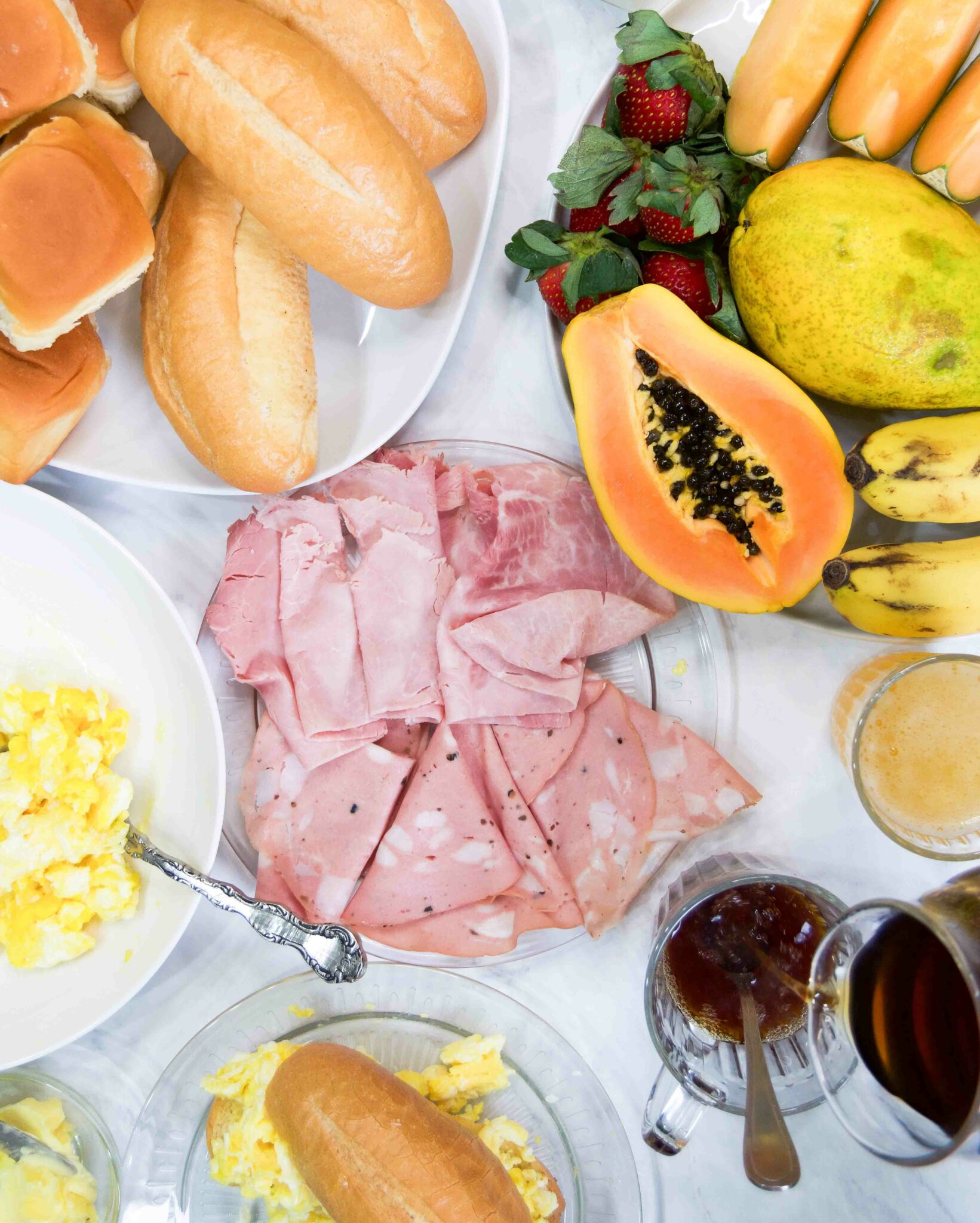 A Brazilian breakfast spread on a table with fresh fruit, cold cuts, coffee and more