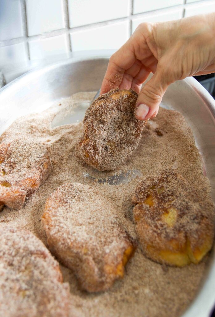 A hand rolls deep fried french toast in cinnamon-sugar