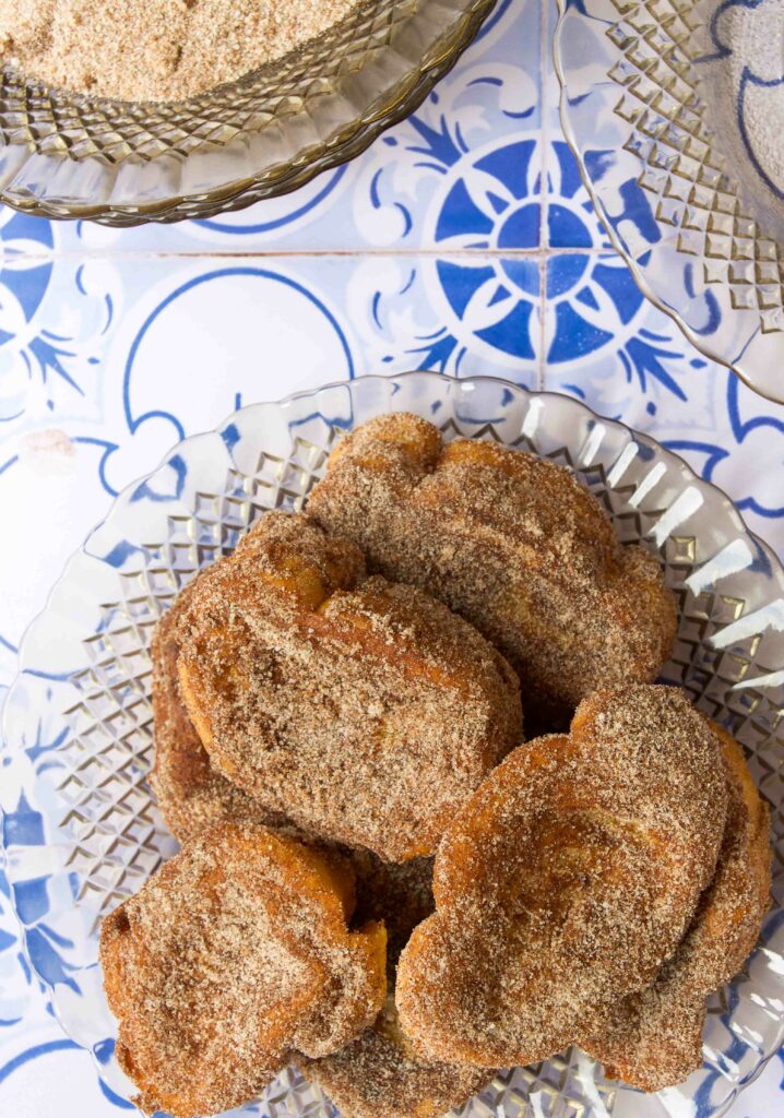 Pieces of cinnamon-sugar coated Rabanada on a glass plate on a blue tile countertop