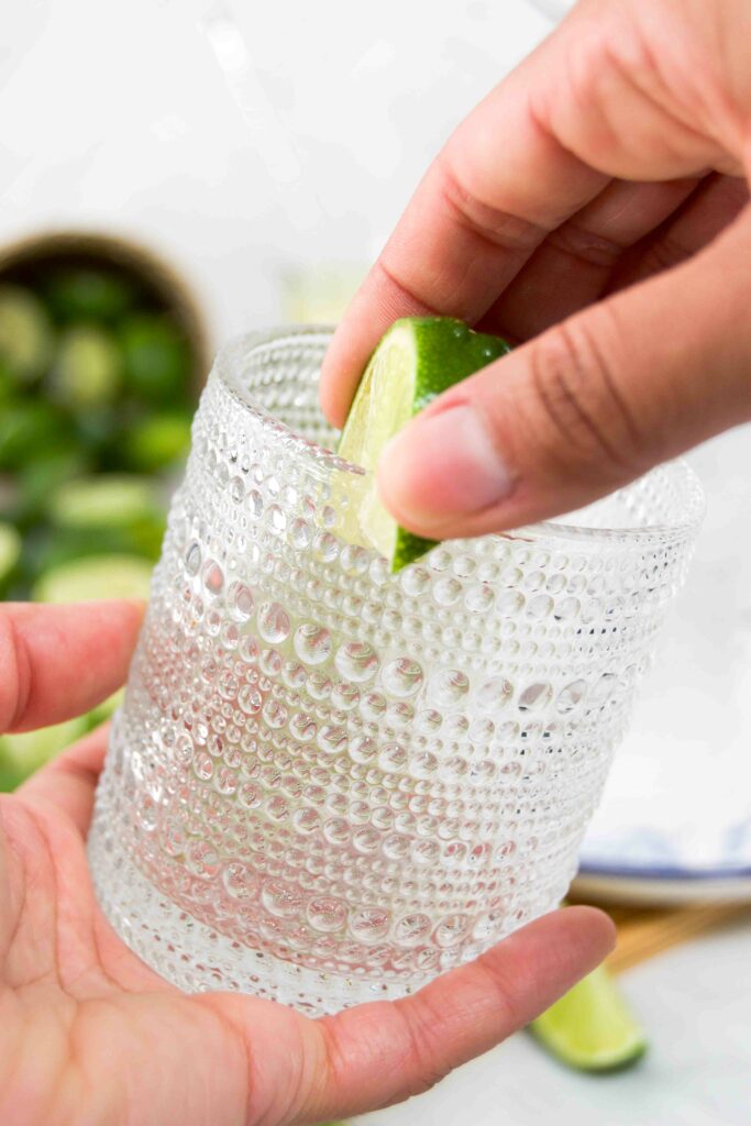 A hand runs a lime wedge along the rim of a glass before adding salt