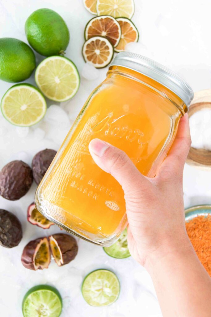 A orange mixed drink in a mason jar is shaken by a hand