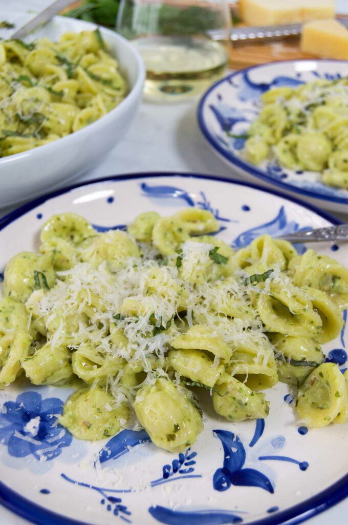 Several blue and white plates of orecchiette with pesto alfredo sauce on a table