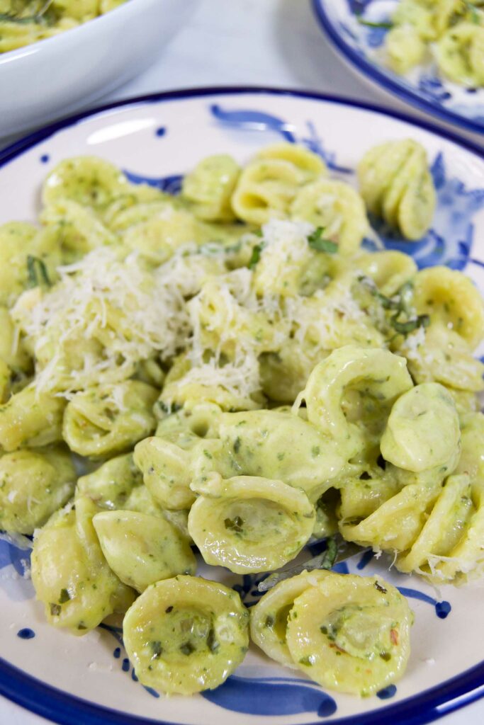 Close up of pesto alfredo sauce on top of orecchiette pasta with additional shredded parmesaon on top