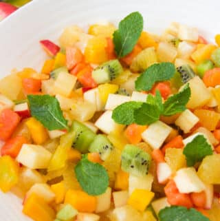 close up of a white bowl holding a serving of tropical fruit salad garnished with mint leaves