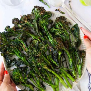 two hands with red nail polish hold a plate of air fryer broccolini after cooking