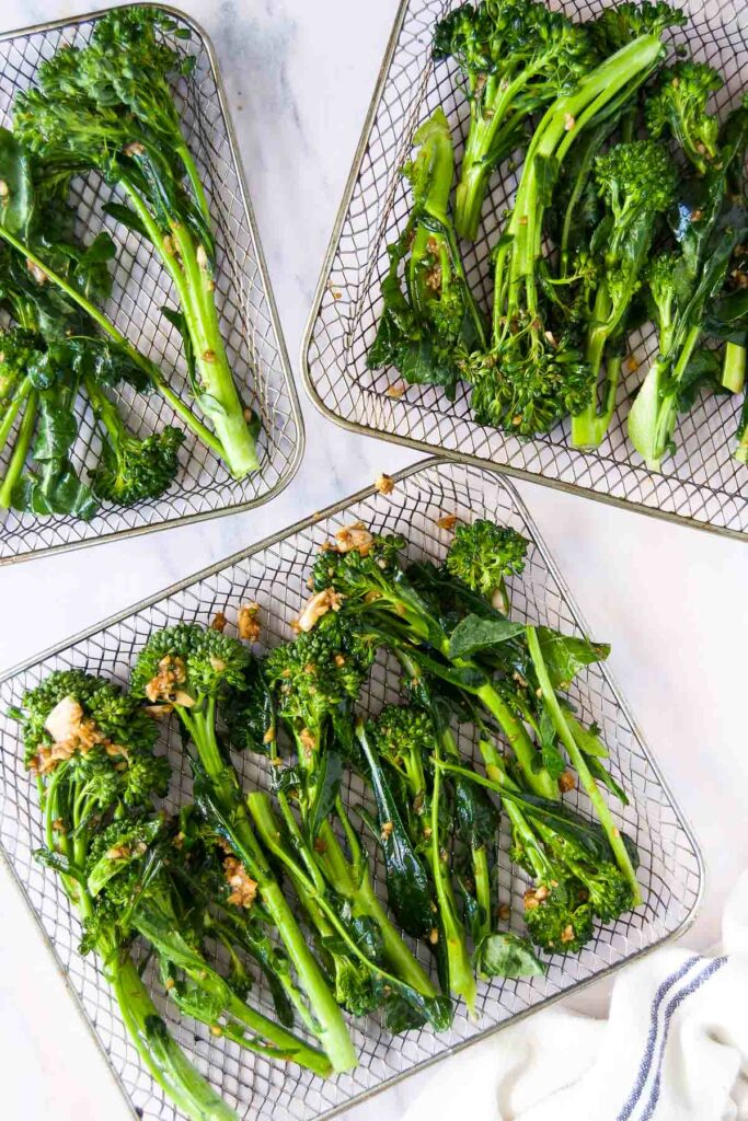 three air fryer baskets holding broccolini before air frying