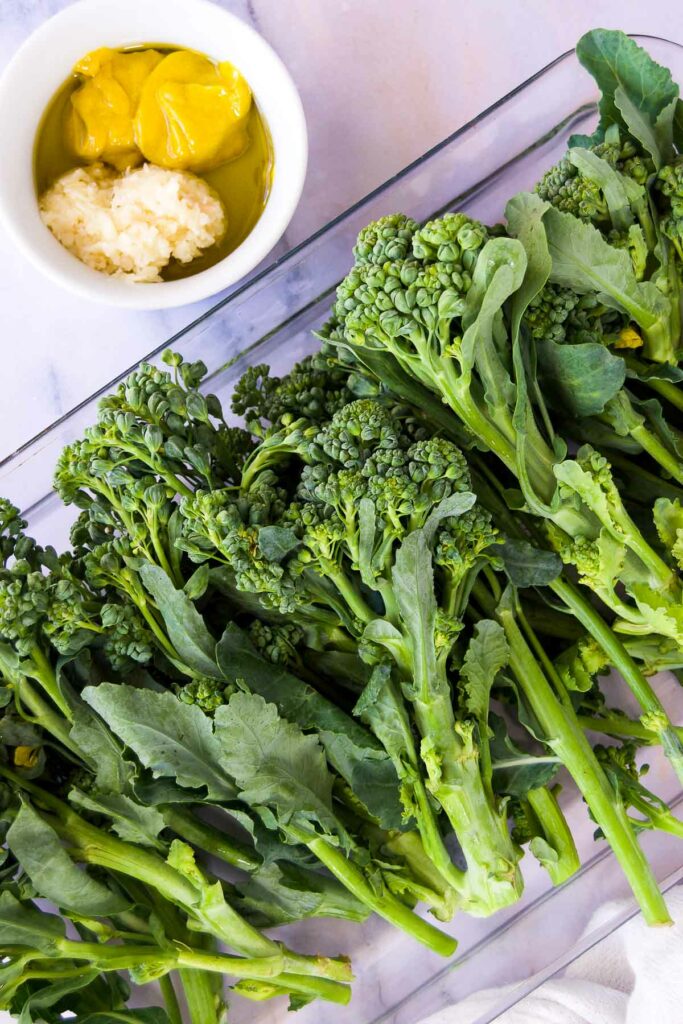 close up of raw broccolini in a casserole dish next to a bowl of seasonings