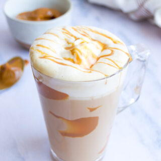 a dulce de leche latte on a marble surface with foam and a dulce de leche drizzle on top