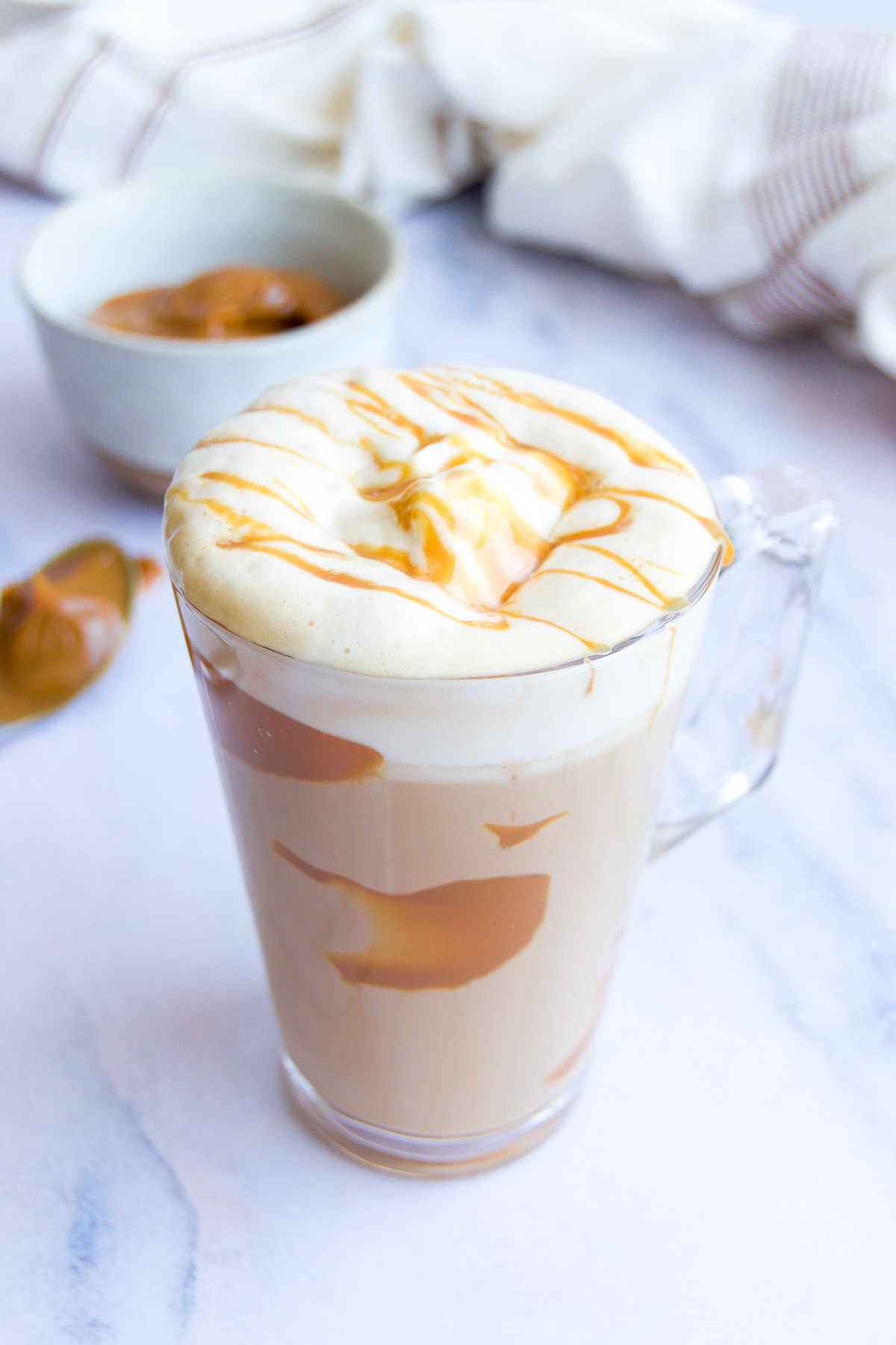 a dulce de leche latte on a marble surface with foam and a dulce de leche drizzle on top