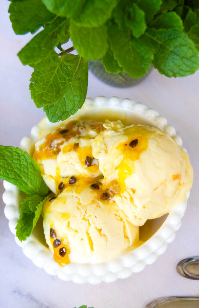 overhead close up of a bowl of passionfruit ice cream garnished with mint leaves and passion fruit puree
