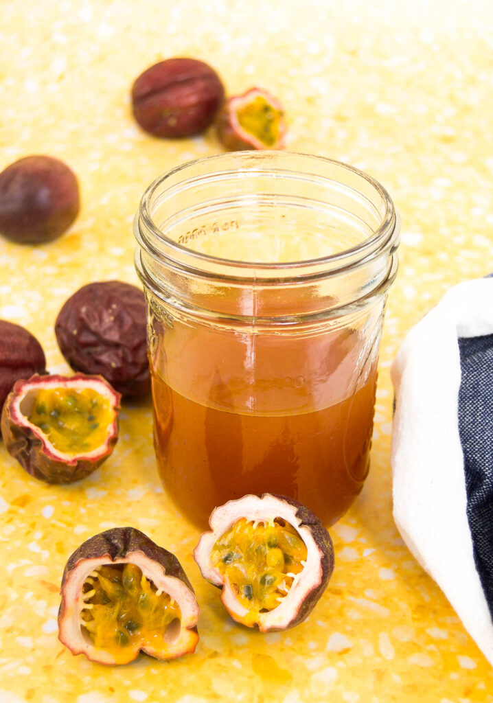 a mason jar of passion fruit sauce in a jar sitting on a yellow surface with purple passion fruits