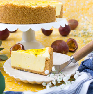 a slice of passion fruit cheesecake on a white plate next to a dish holding the rest of the no bake cheesecake on a yellow surface