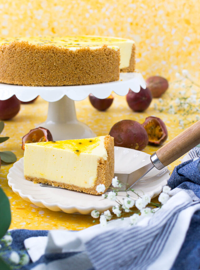 a slice of passion fruit cheesecake on a white plate next to a dish holding the rest of the no bake cheesecake on a yellow surface