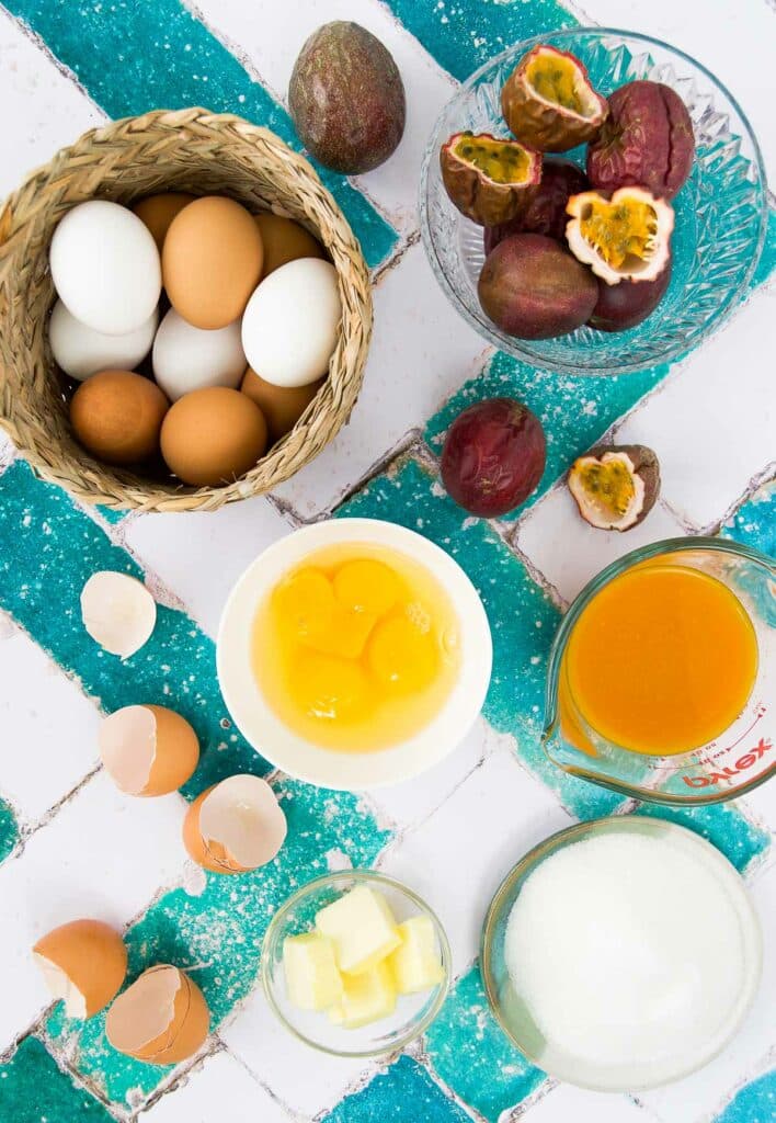 ingredients to make passion fruit curd in bowls and cups with fresh passionfruits on a teal and white tiled surface