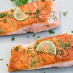 two pieces of seared salmon on a plate garnished with lemon and fresh chopped herbs