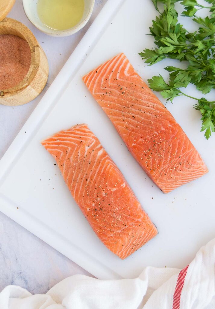 two pieces of seasoned salmon on a cutting board before cooking