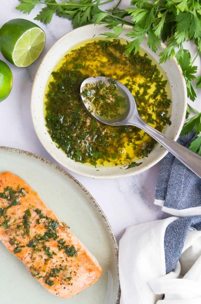 a small bowl of lime butter sauce for fish with a spoon in it next to a plate with seared salmon