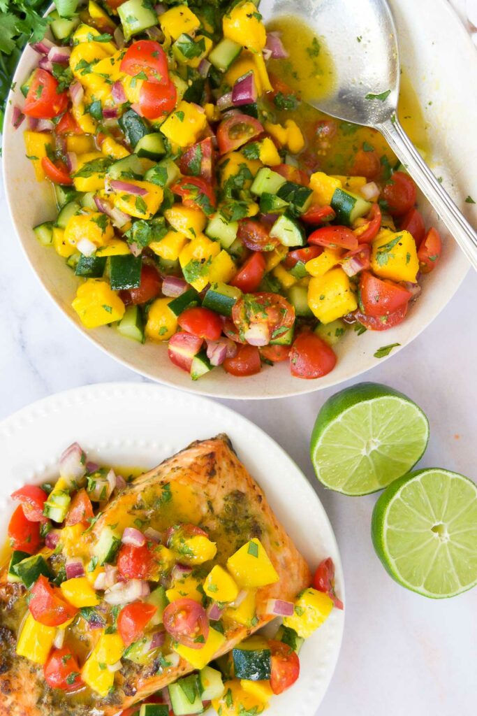 a bowl of cucumber mango salsa next to a plate of salmon