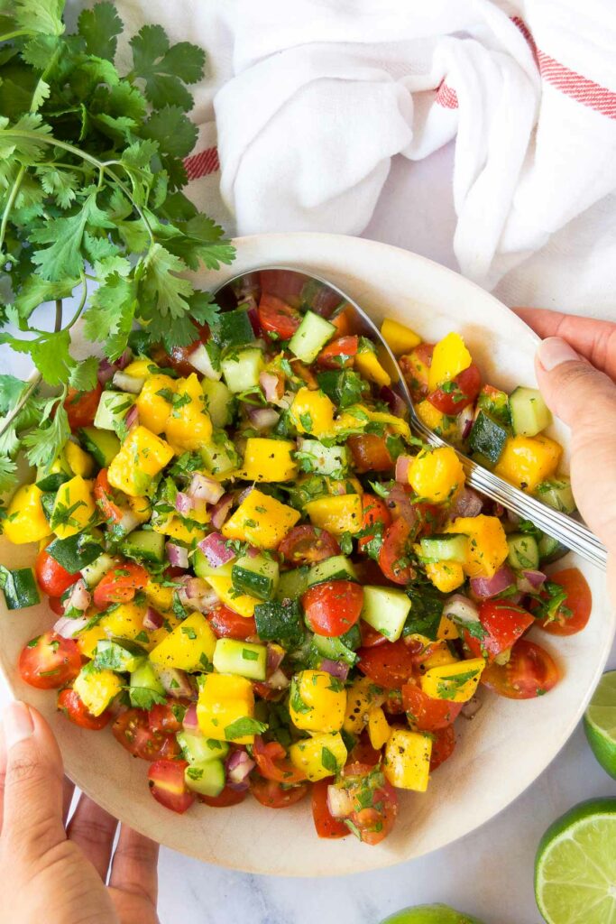 two hands hold a bowl of bright cucumber mango salsa